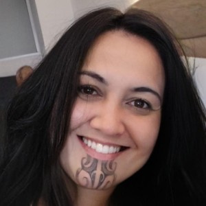 Headshot of Māori woman with long dark hair, moko kauae (sacred Māori chin tattoo) and smiling.